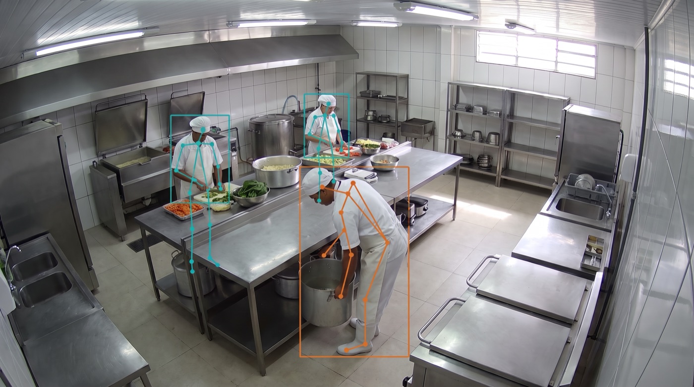 Câmera de segurança de uma cozinha industrial: cozinheiro curvado levantando uma panela destacado em laranja