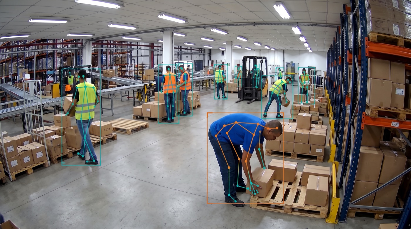 Câmera de segurança de um centro de distribuição: trabalhador de camiseta azul curvado sobre um palete, o único sem colete refletivo, destacado pela IA